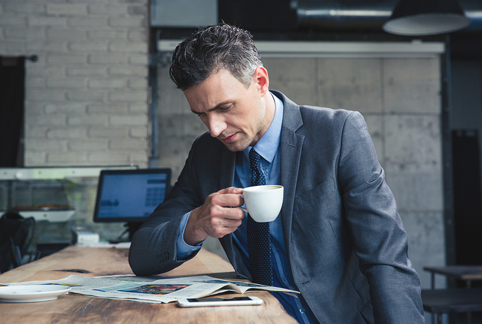 Ejecutivo leyendo periódico en una cafetería tomando un café